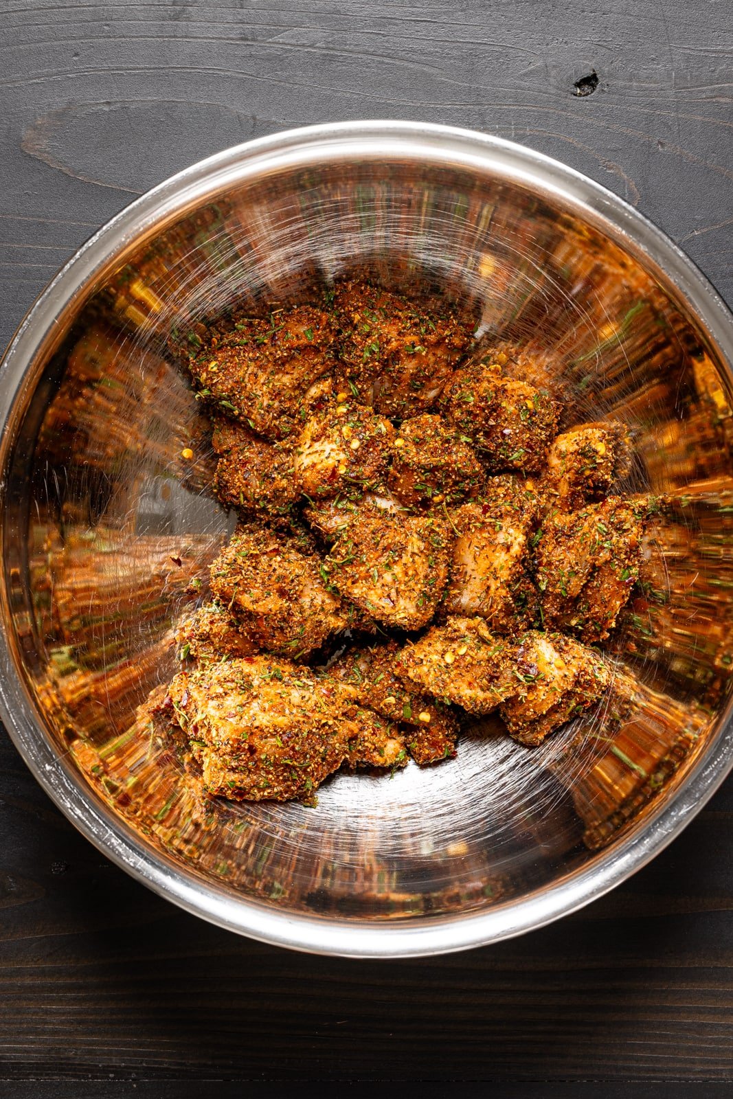 Seasoned chicken pieces in a large silver bowl.