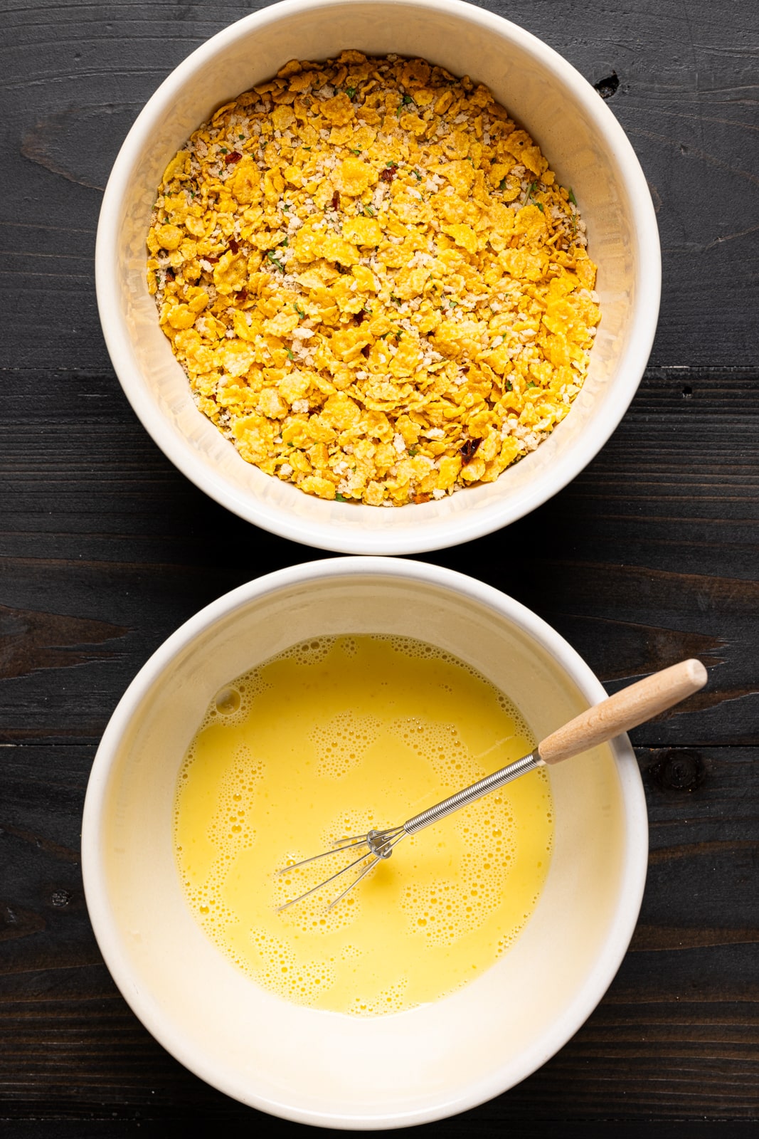 Two white bowls with breadcrumbs and egg batter with a whisk.