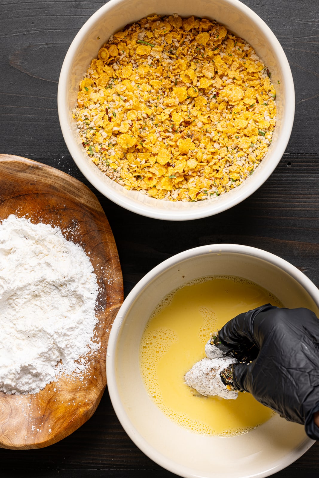 Chicken being dipped in egg batter along with flour and breadcrumbs.