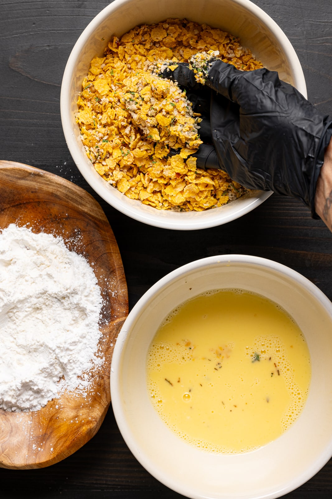 Chicken piece being rolled in breadcrumbs with bowls of flour and egg batter.