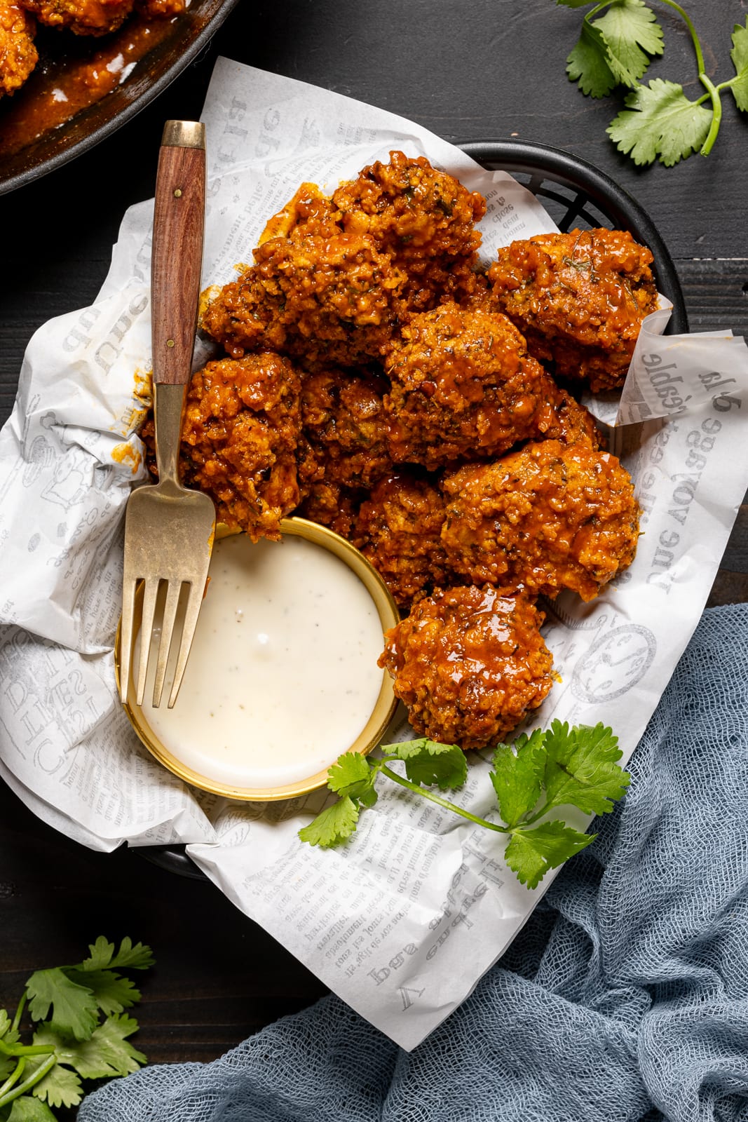 Chicken in a basket with a fork and dipping sauce and herbs.