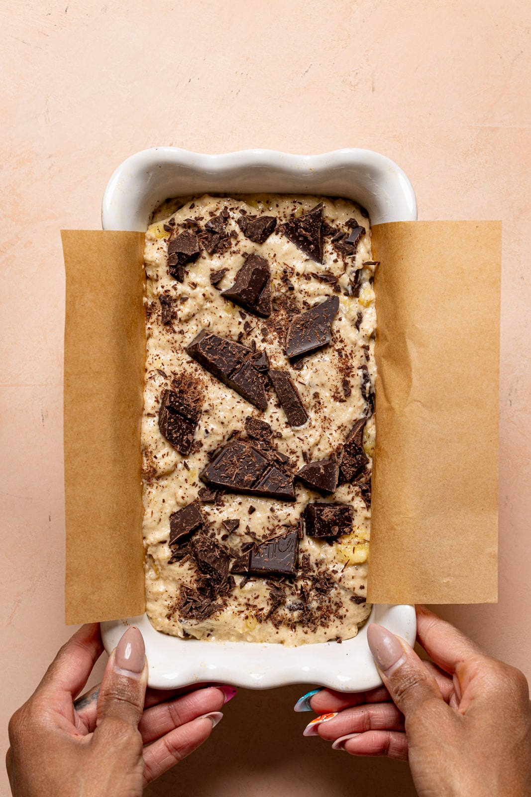 Vegan Batter in a loaf pan with parchment paper and chopped chocolate on top.