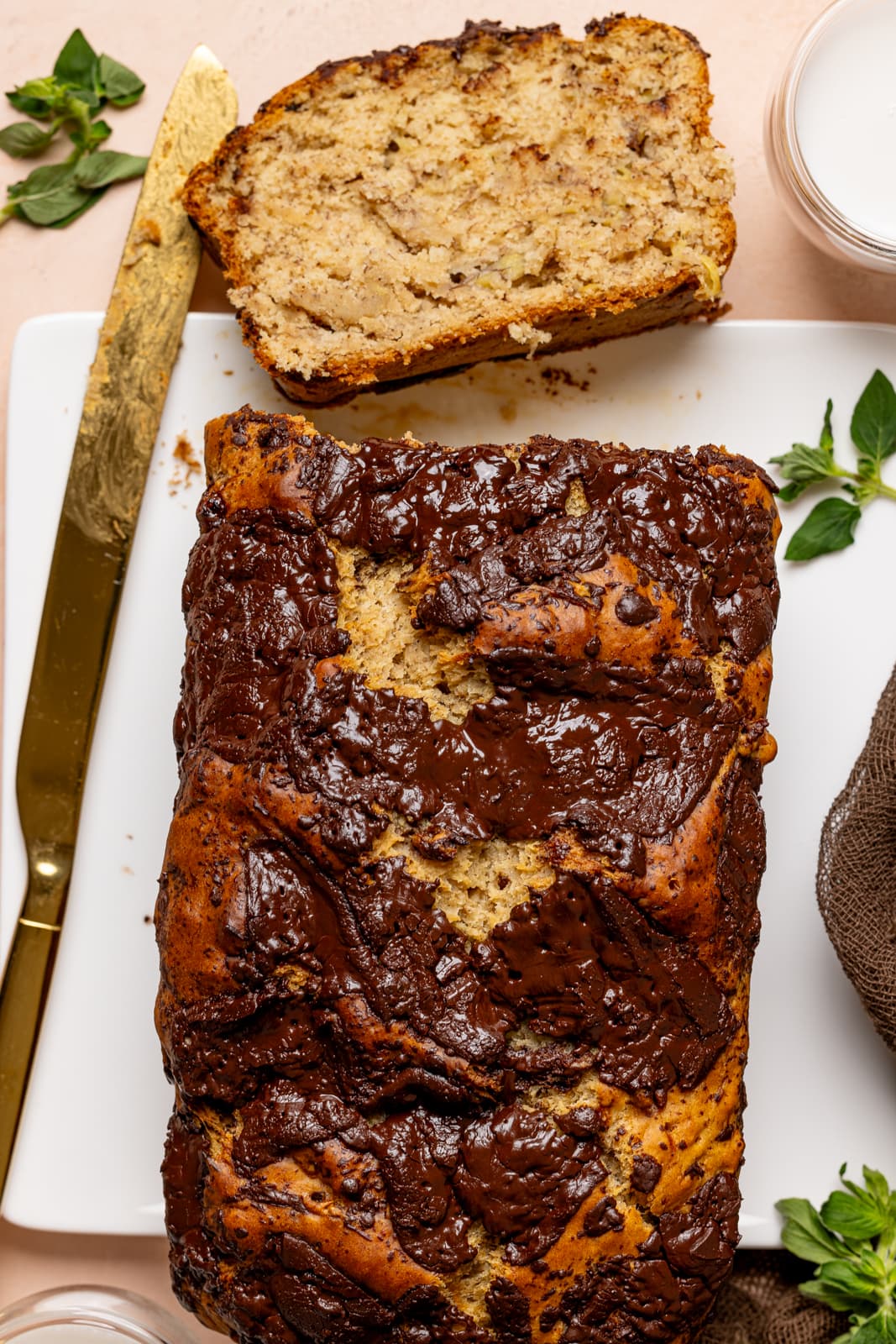 Maple Chocolate Chip Banana Bread. Baked bread on a white plate sliced with a gold knife and glass of milk.