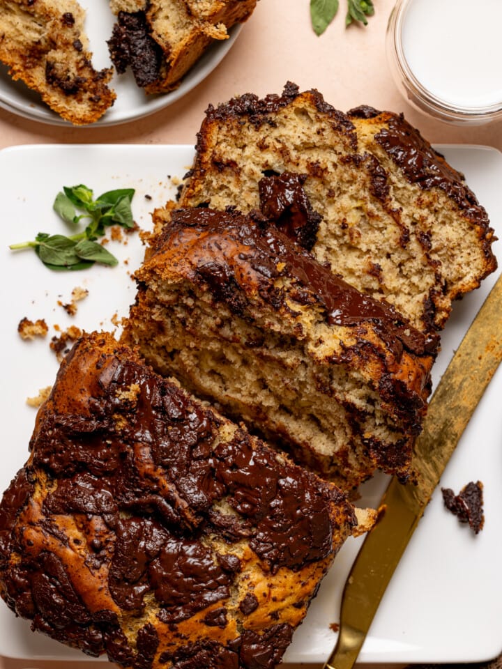 Baked bread with slices on a white plate with a knife and milk.