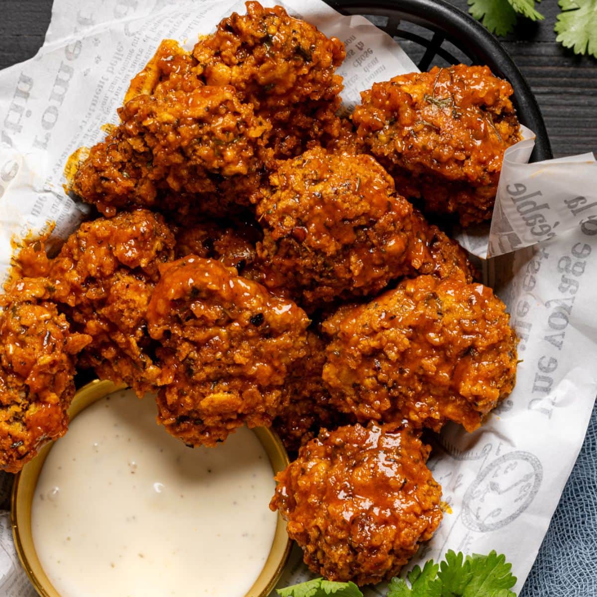 Up close shot of chicken in a basket with dipping sauce and fresh herbs.