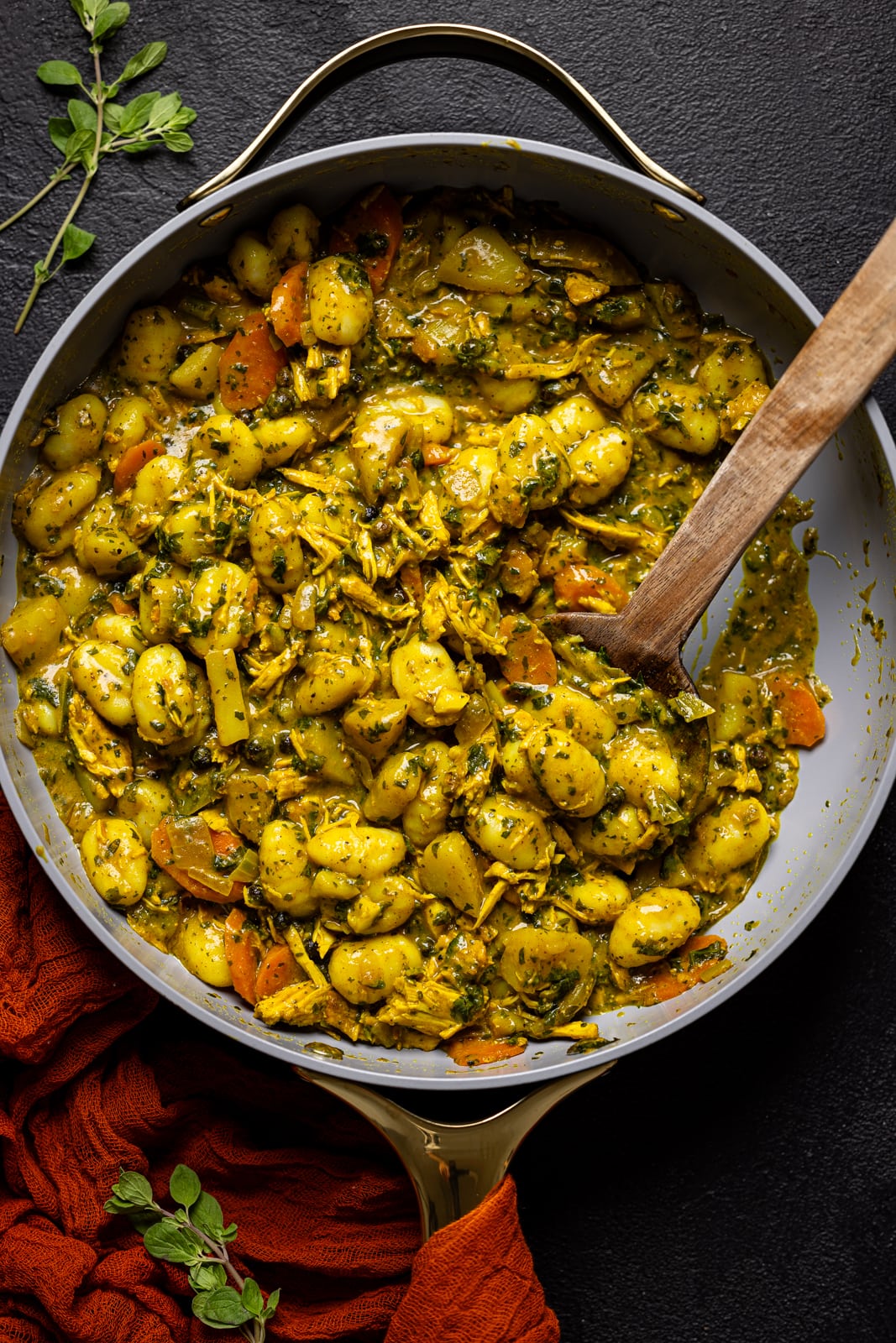 Curry chicken and gnocchi in a skillet with a wooden spoon.