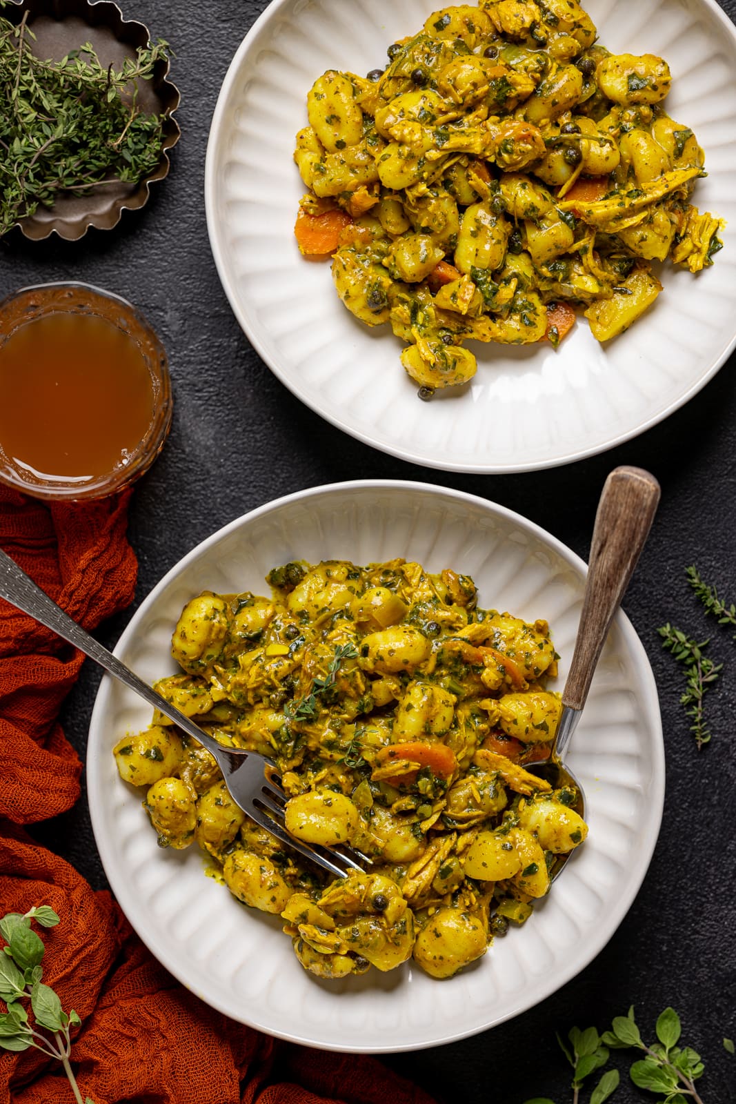 Two bowls of chicken + gnocchi with a fork and spoon with a side of juice.