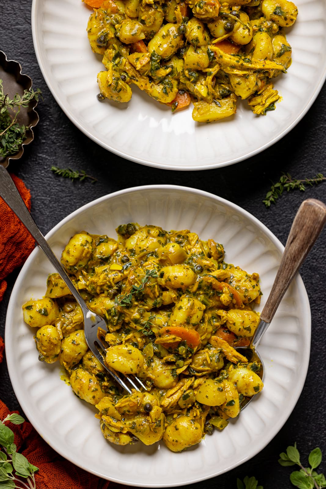 Two bowls of chicken and gnocchi on a black table.