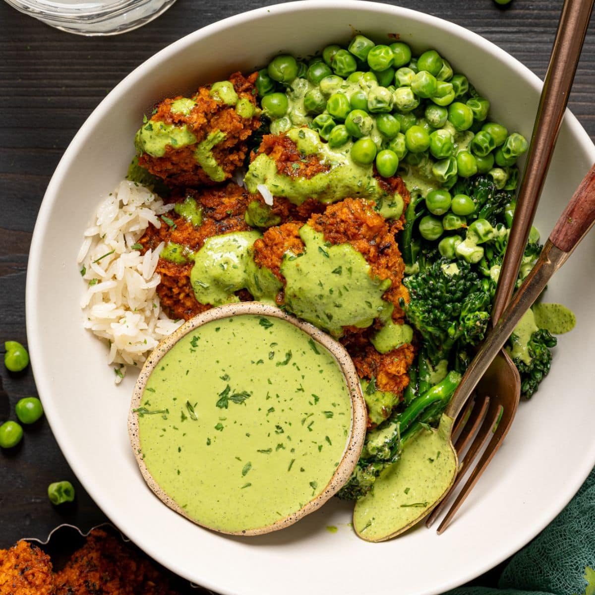 Up close shot of chicken bowl with a glass of juice and green peas.