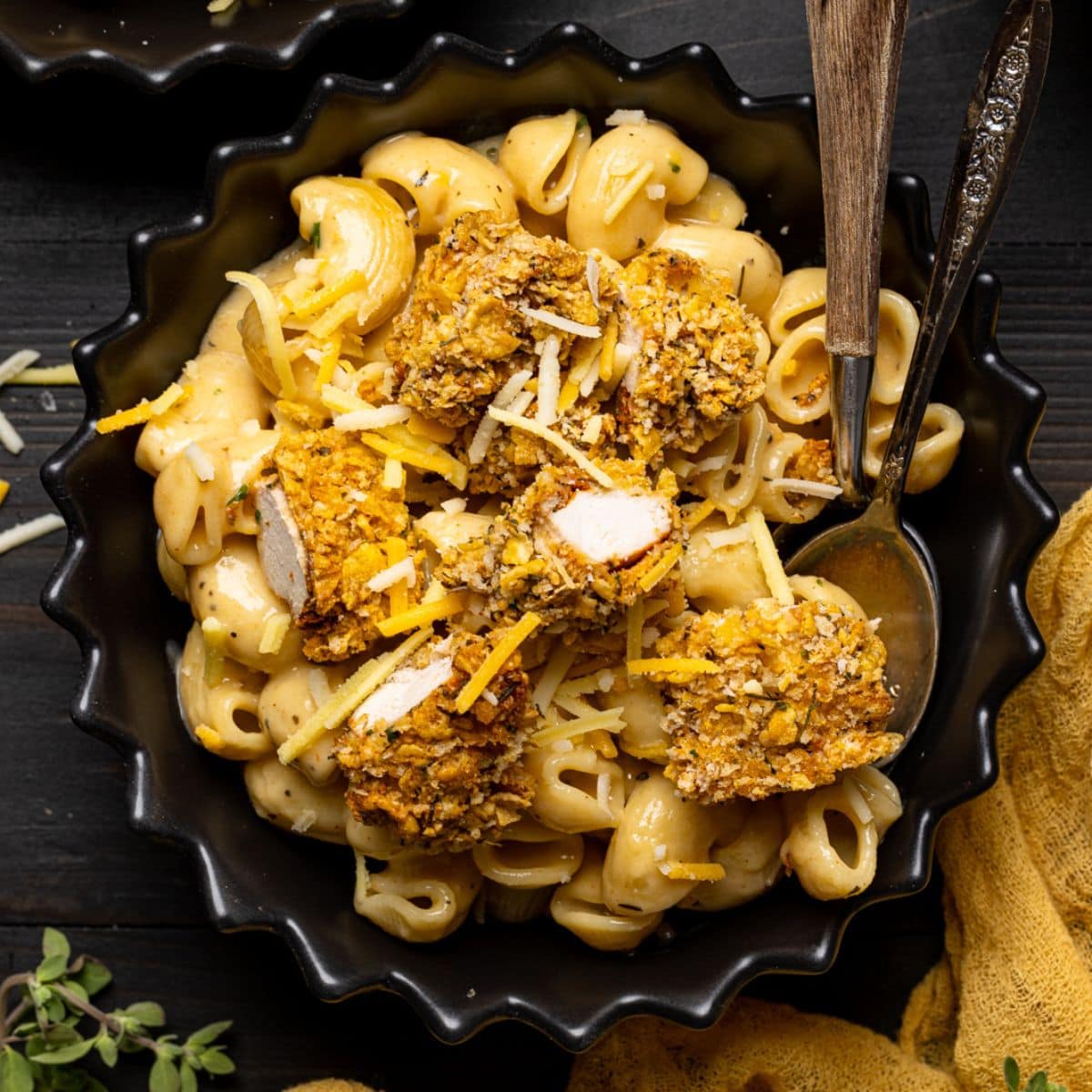 Chicken and mac + cheese in a black bowl with two spoons and a yellow napkin.