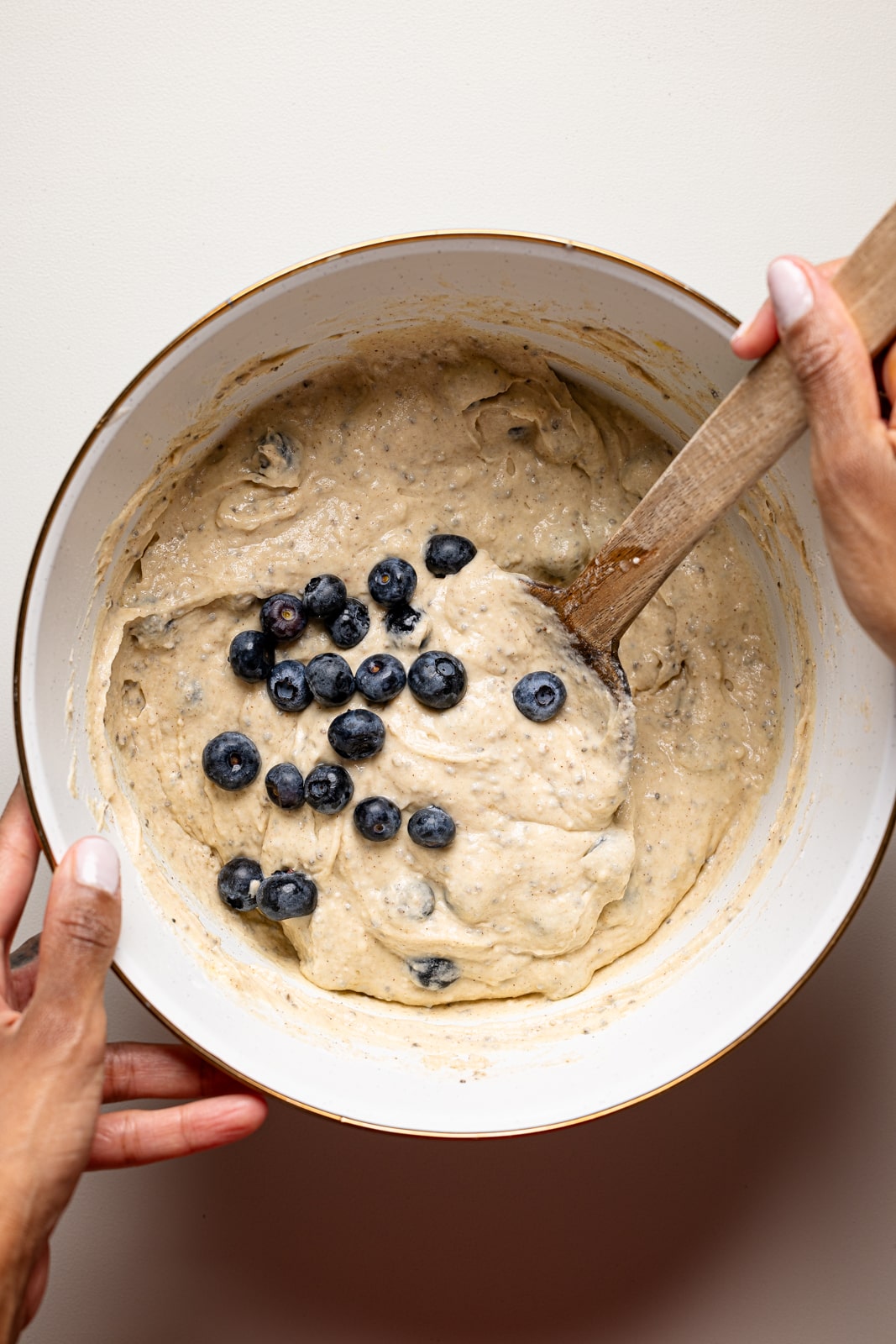 Pancake batter in a bowl with a wooden spoon and blueberries.