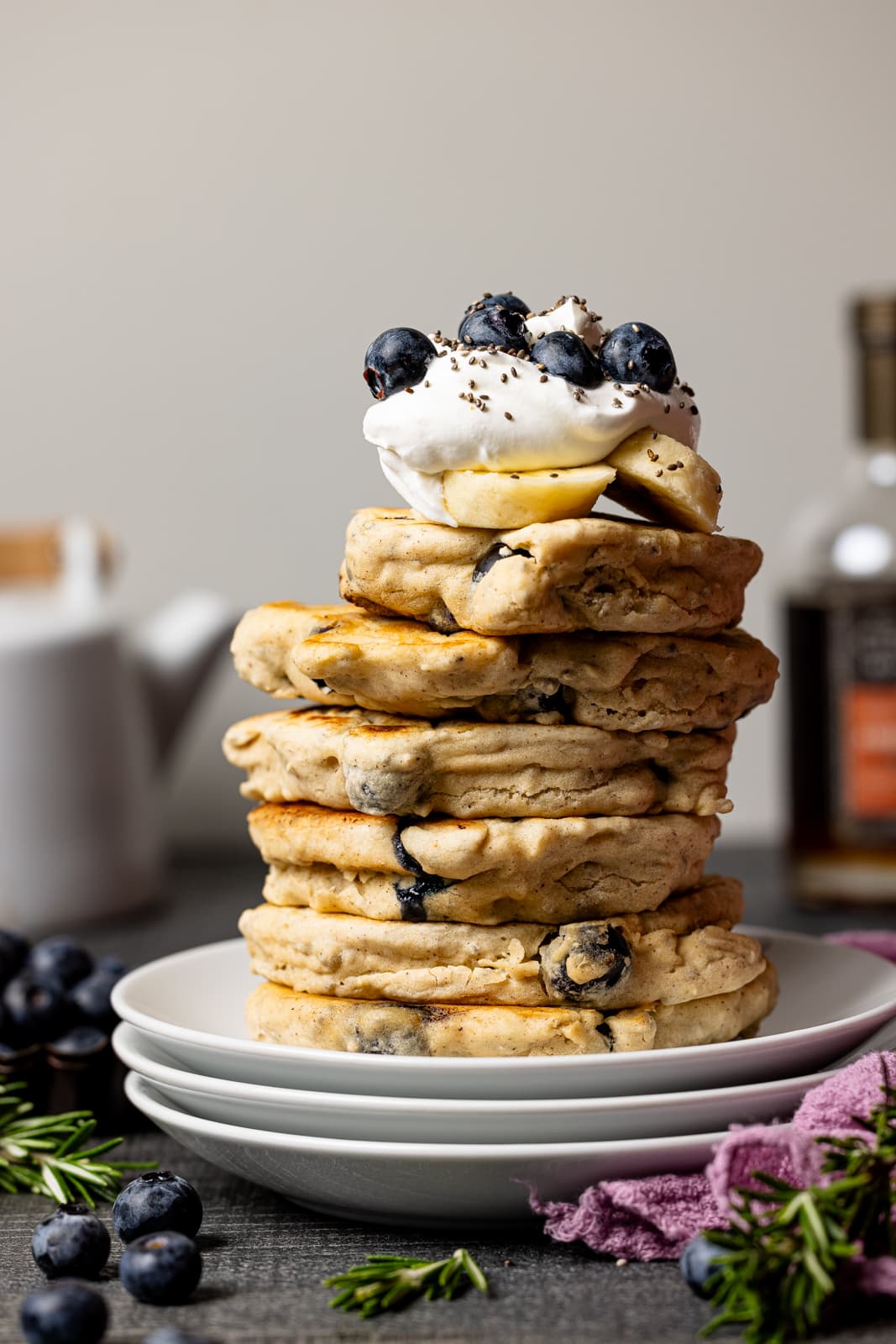 Stack of pancakes on three plates with blueberries and maple syrup in the background. 