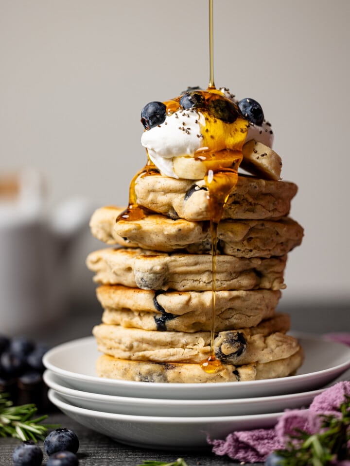 Drizzle of maple syrup atop stacks of pancakes on three stacks of plates.