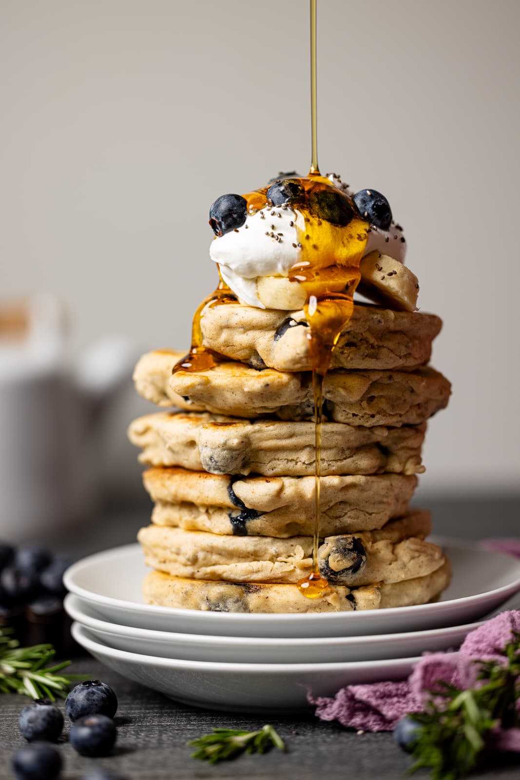 Drizzle of maple syrup atop stacks of pancakes on three stacks of plates. 
