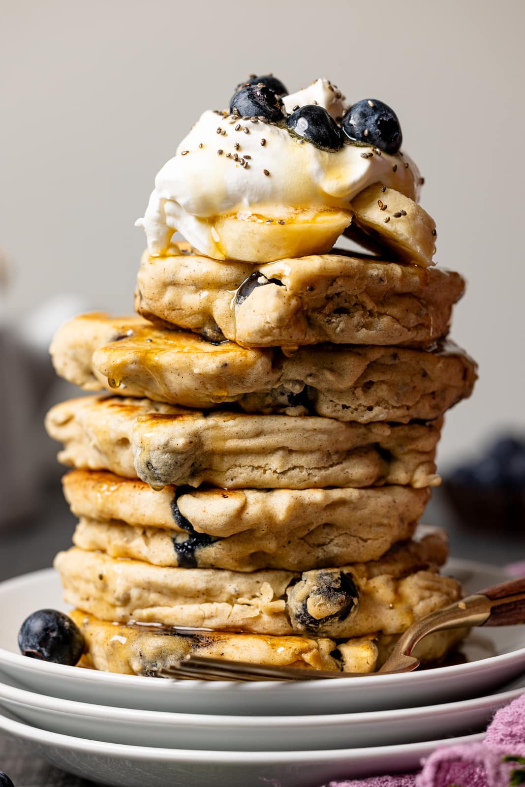 Stack of pancakes on three white plates with whipped cream and blueberries.