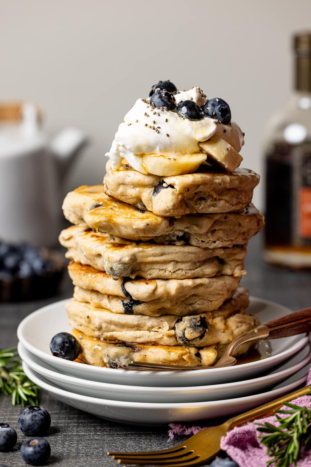 Stacks of pancakes on white plates with a forks and maple syrup. 