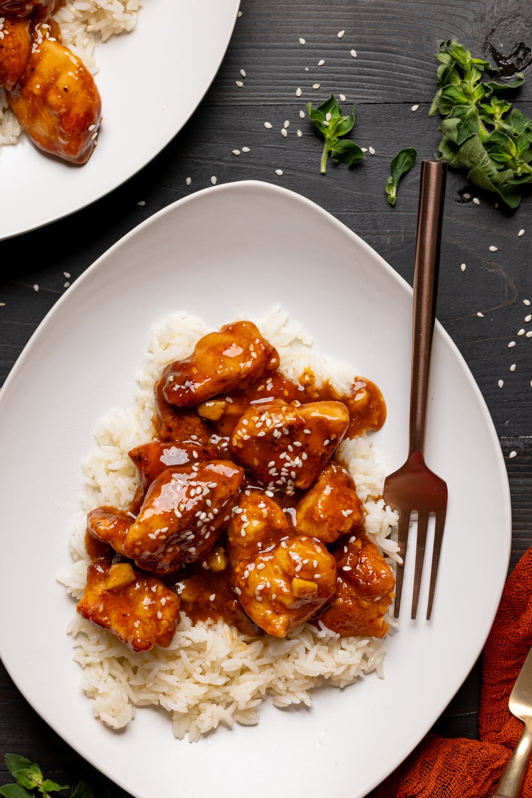 Two plates with chicken and rice with a fork and herbs.