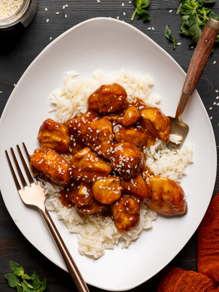 Chicken and rice in a plate with two forks on a black table.