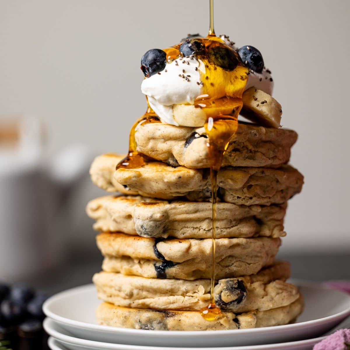 Drizzle of maple syrup atop stacks of pancakes on three stacks of plates.
