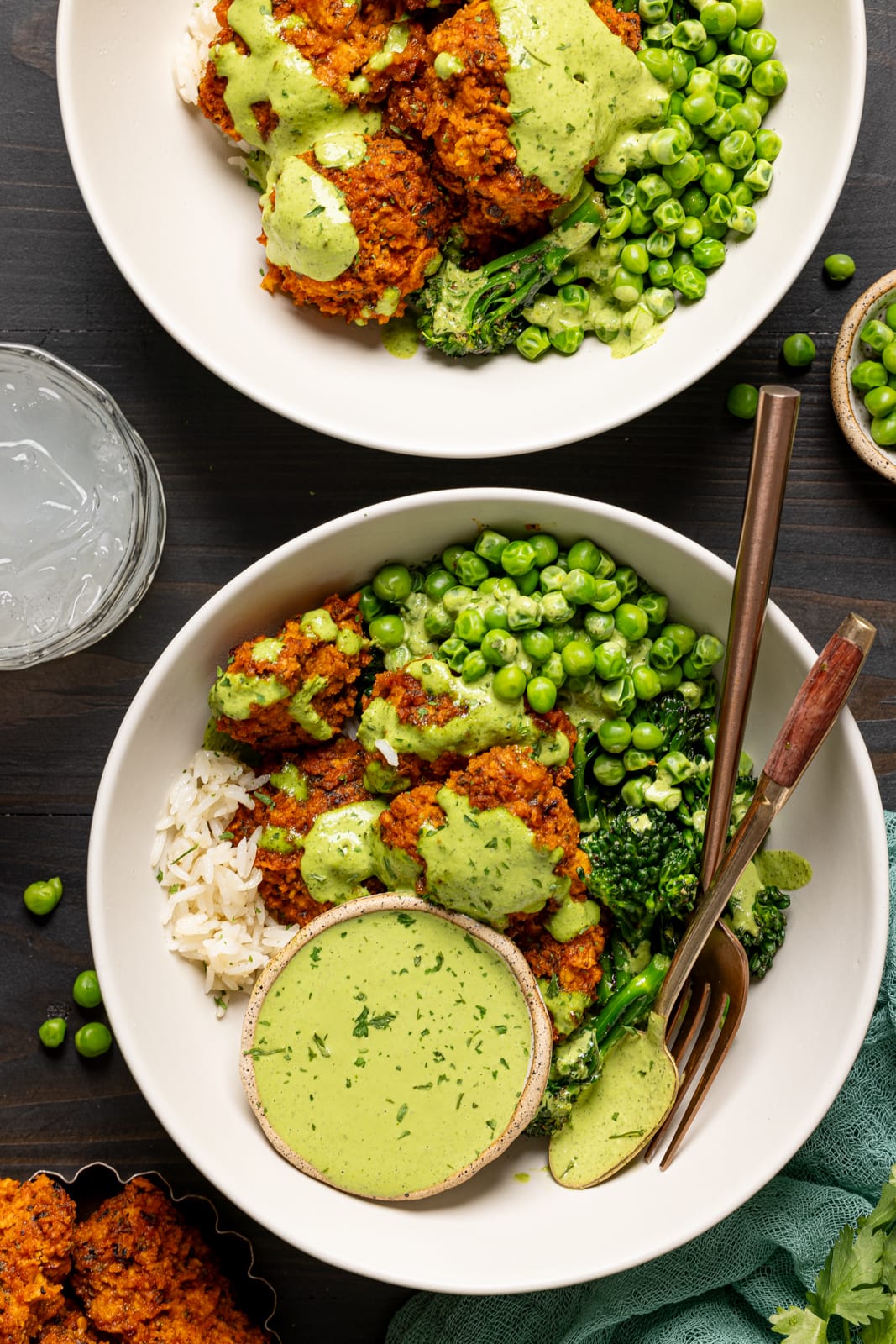 Two chicken bowls on a black wood table with green goddess sauce. 