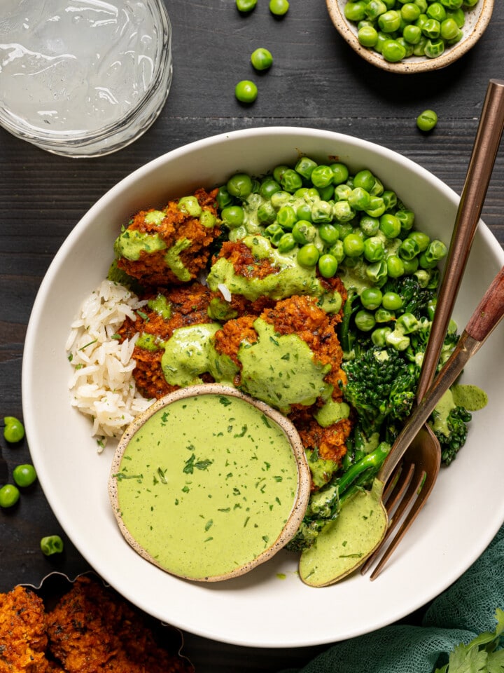 Up close shot of chicken bowl with a glass of juice and green peas.