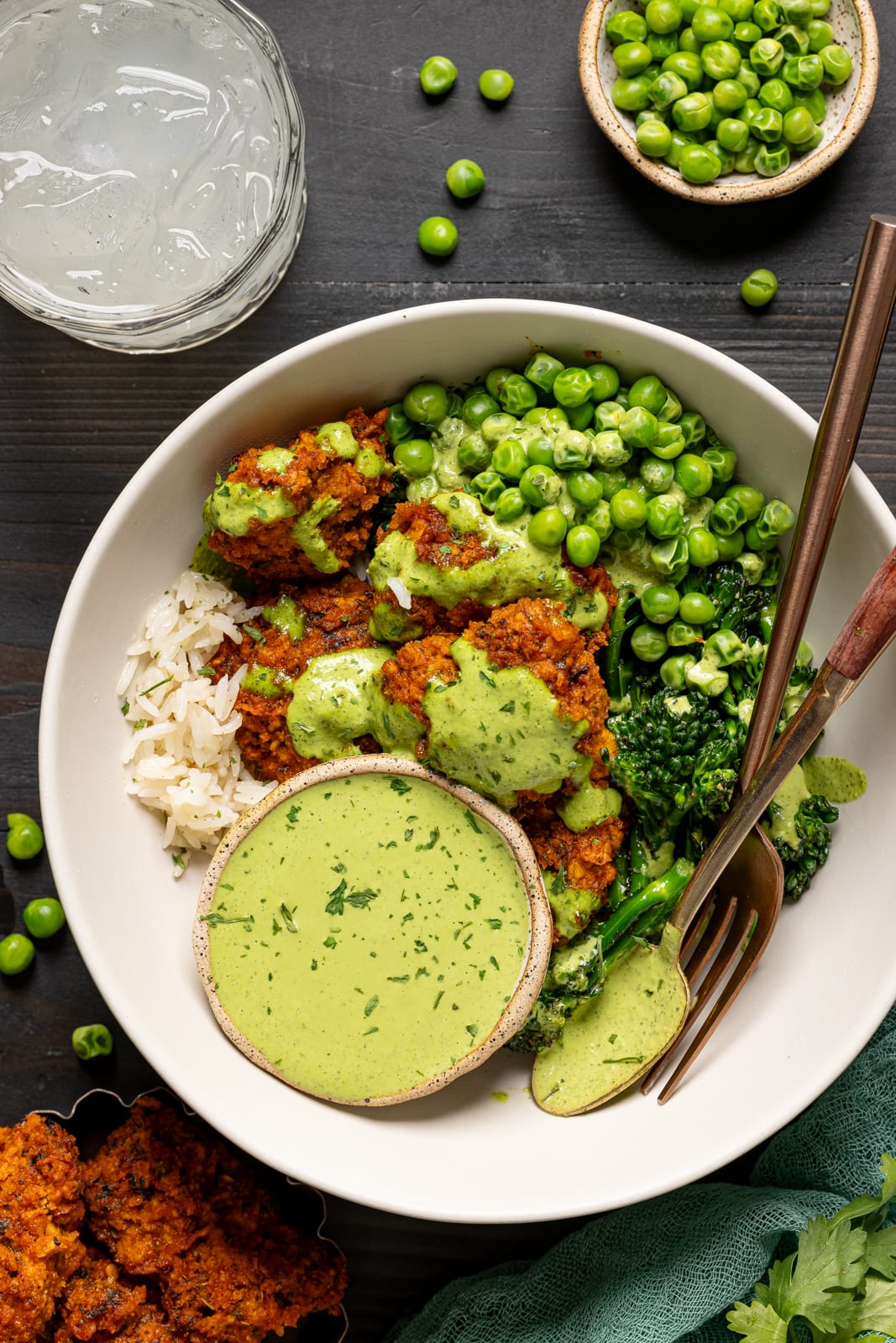 Up close shot of chicken bowl with a glass of juice and green peas.