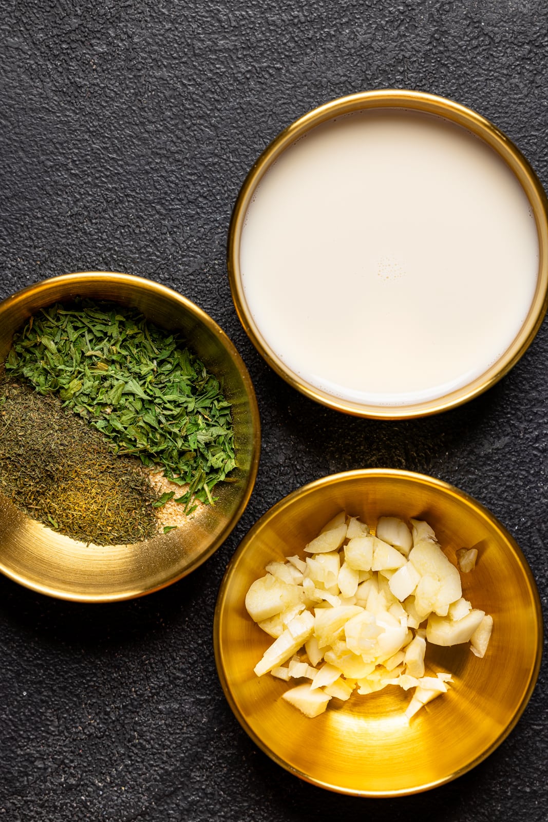 Ingredients on a table including minced garlic, milk, and herbs + seasonings. 