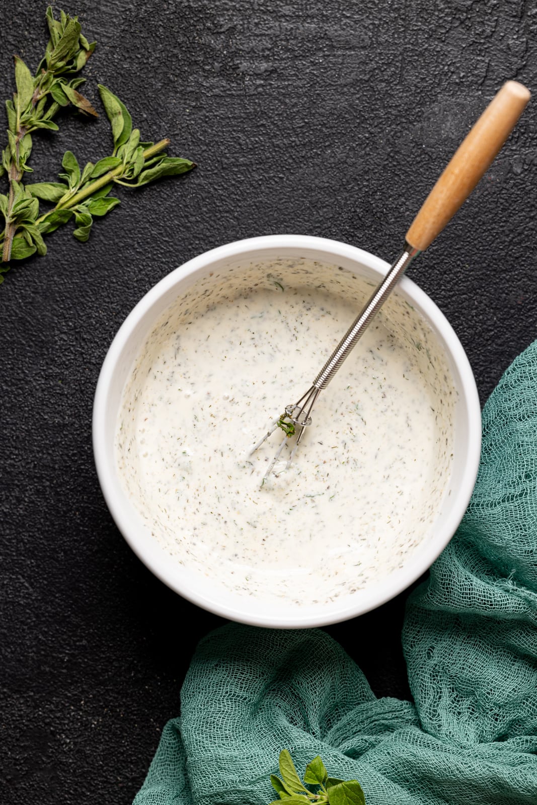 Ranch dressing in a white bowl on a black table with a whisk.