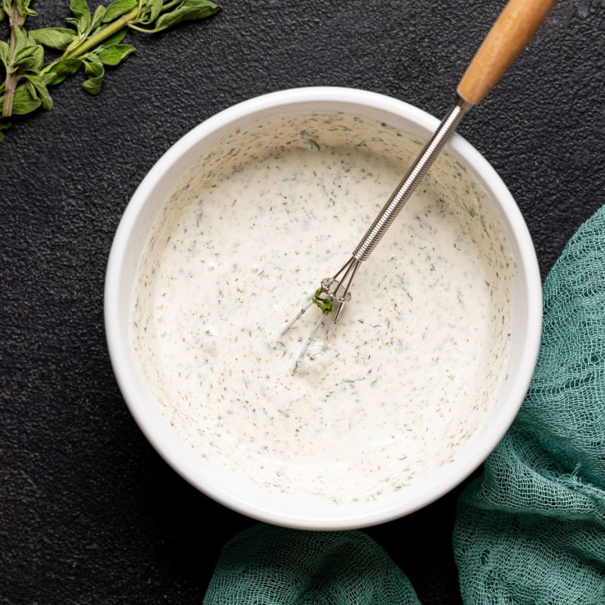 Ranch dressing in a white bowl on a black table with a whisk.