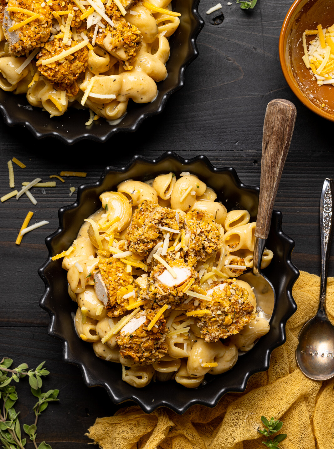 Two bowls of chicken and mac and cheese with a spoon and herbs.