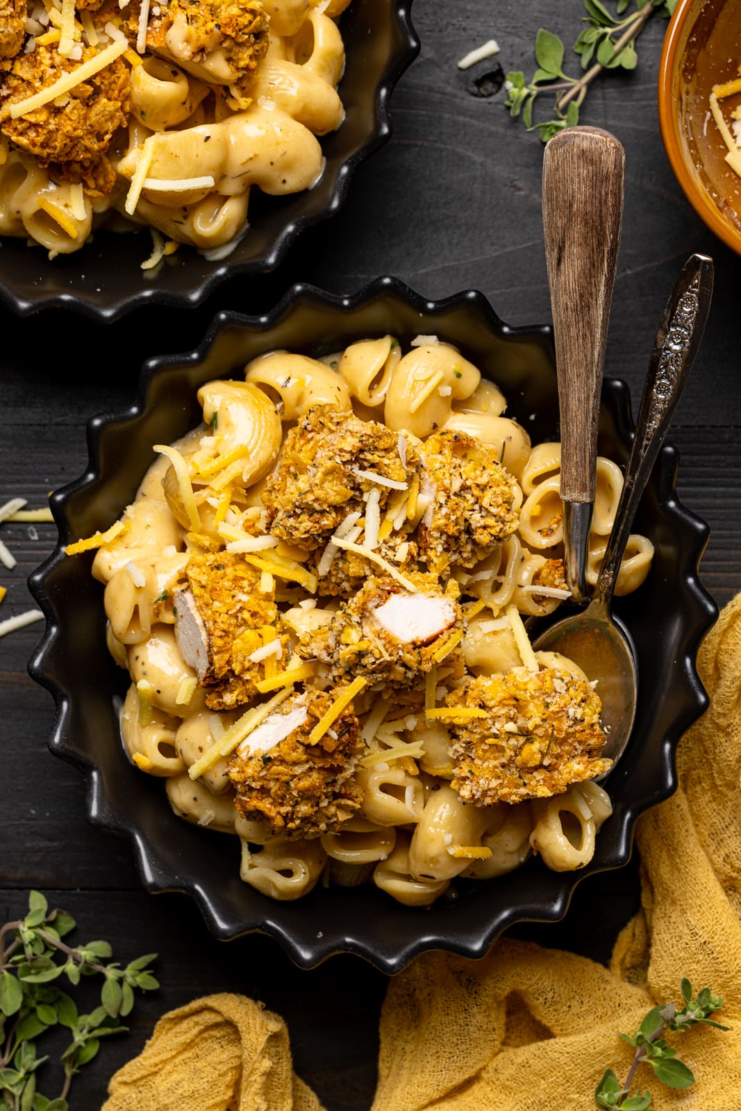 Chicken and mac + cheese in a black bowl with two spoons and a yellow napkin.