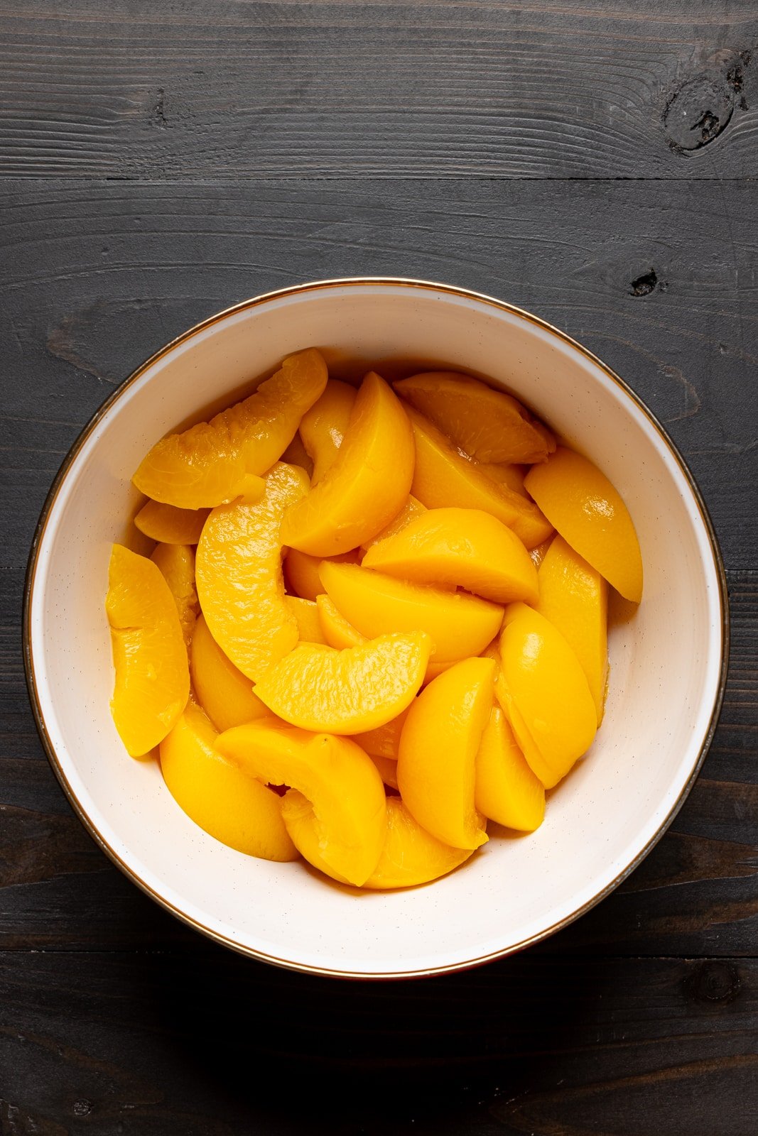 Peaches in a white bowl on a black wood table. 