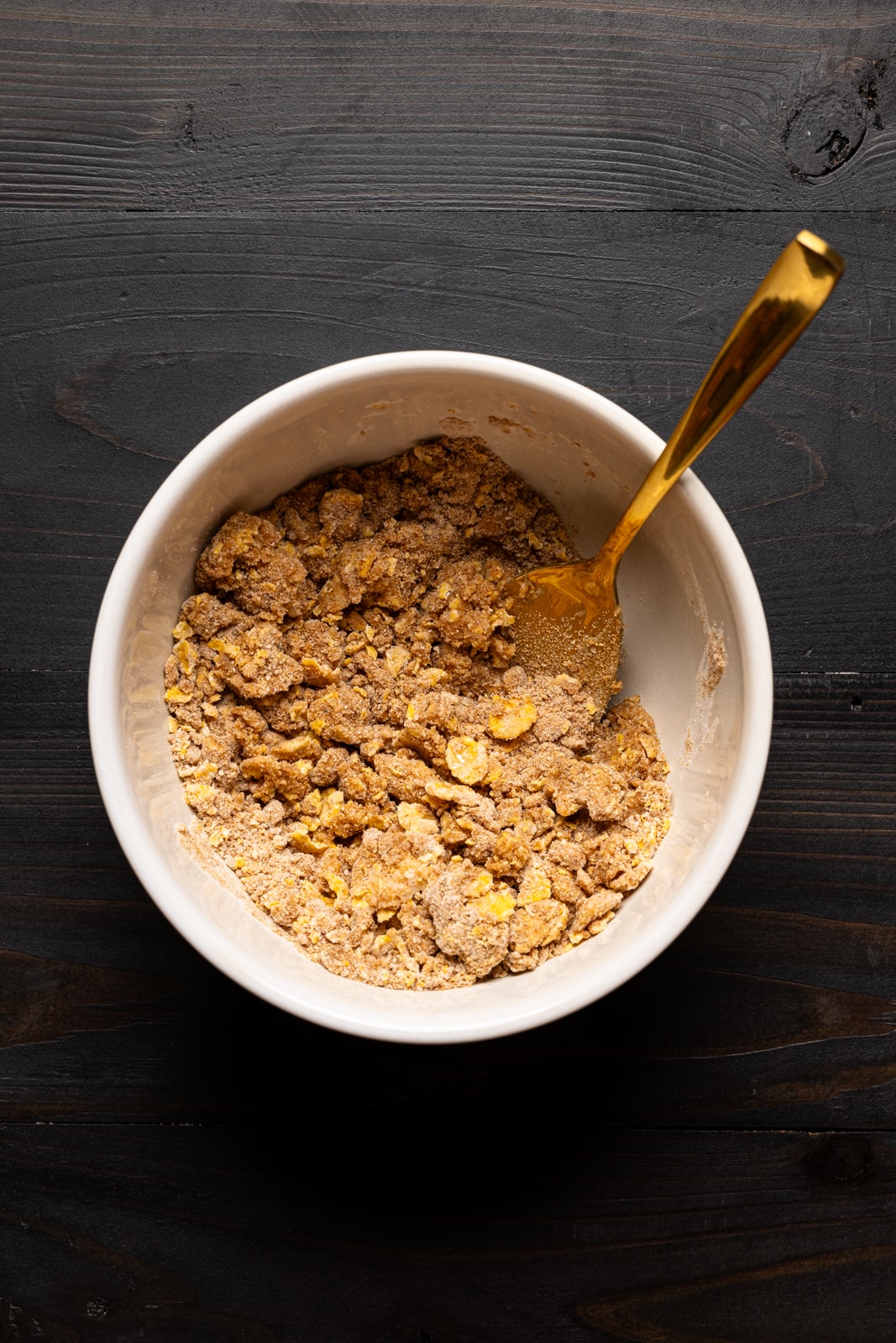 Bowl with dry ingredients on a black wood table with a gold spoon.