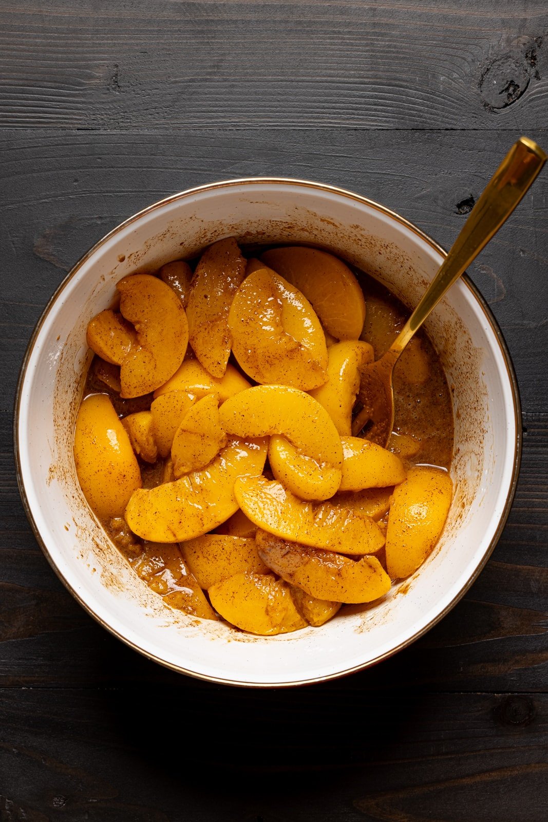 Peaches mixed together with spices and ingredients in a bowl.