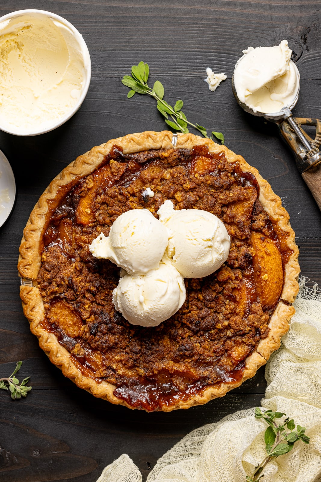 Peach pie with three scoops of ice cream with an ice cream scooper and herbs. 