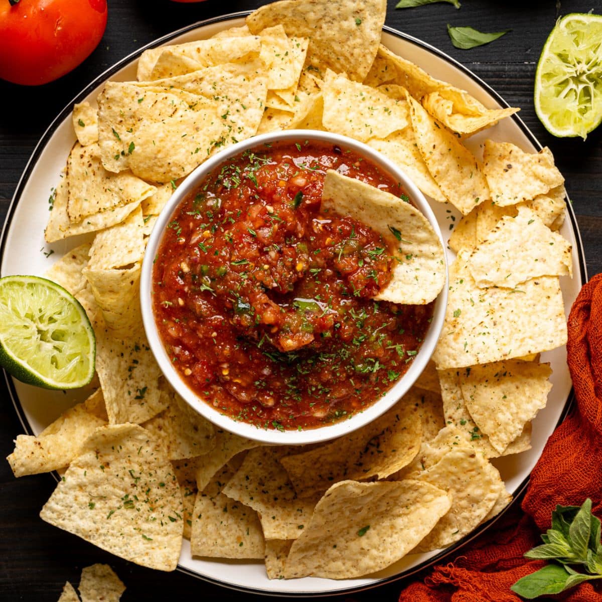 Salsa and chips with tomatoes, lime, and garnish.