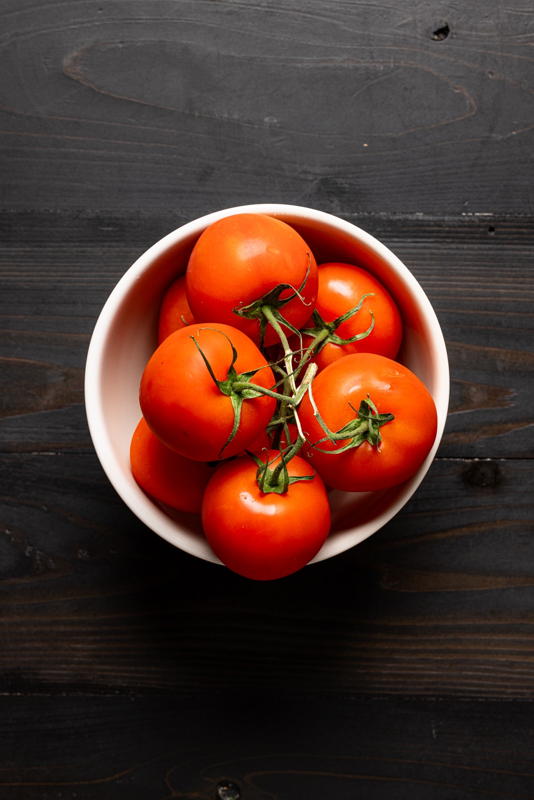 Tomatoes in a bowl on a black table.