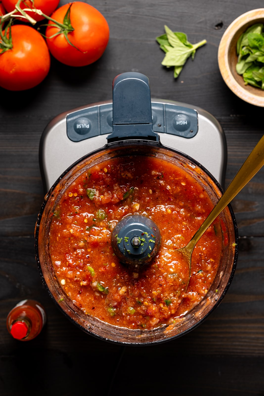 Tomatoes in a food processor with a spoon.