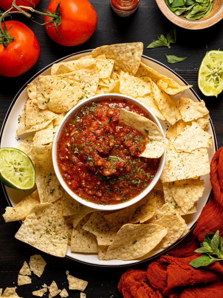 Salsa and chips with tomatoes, lime, and garnish.