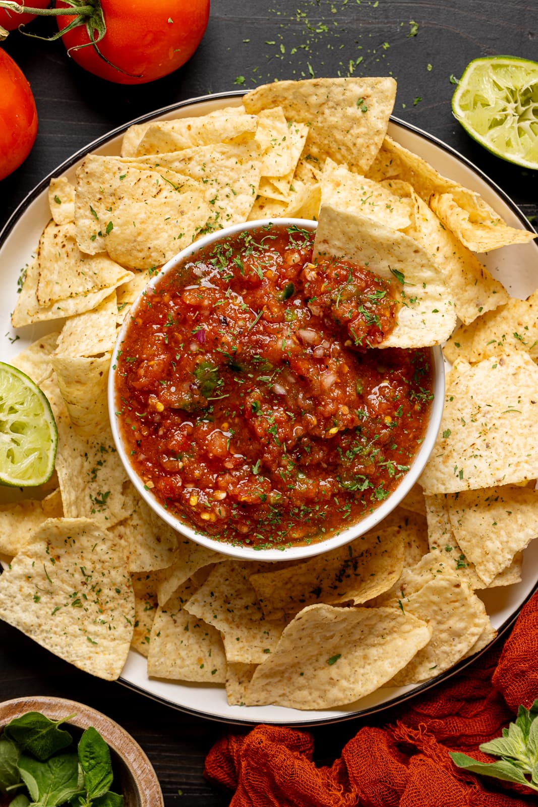 Up close shot of salsa and chips with lime, tomatoes, and garnish.