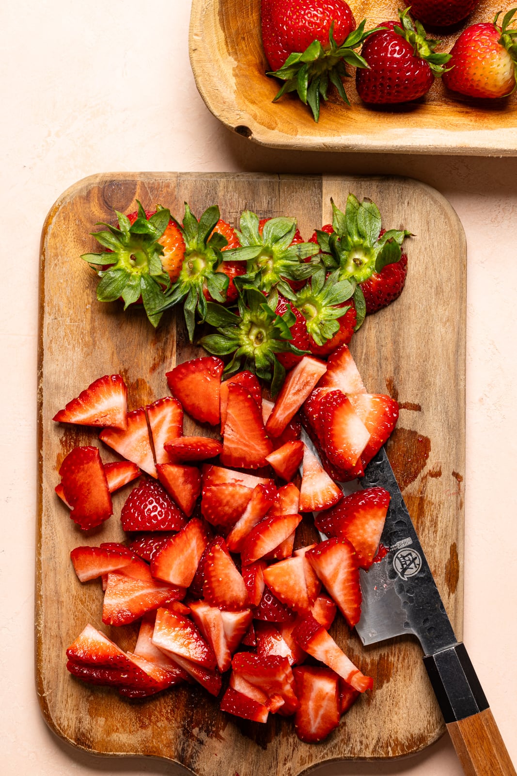 Diced strawberries on a brown cutting board with a knife. 
