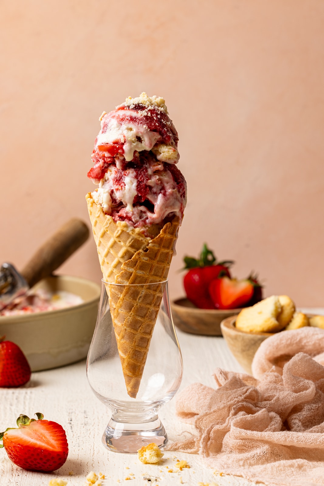 Ice cream cone in a short glass with strawberries and cookies with a peach background. 