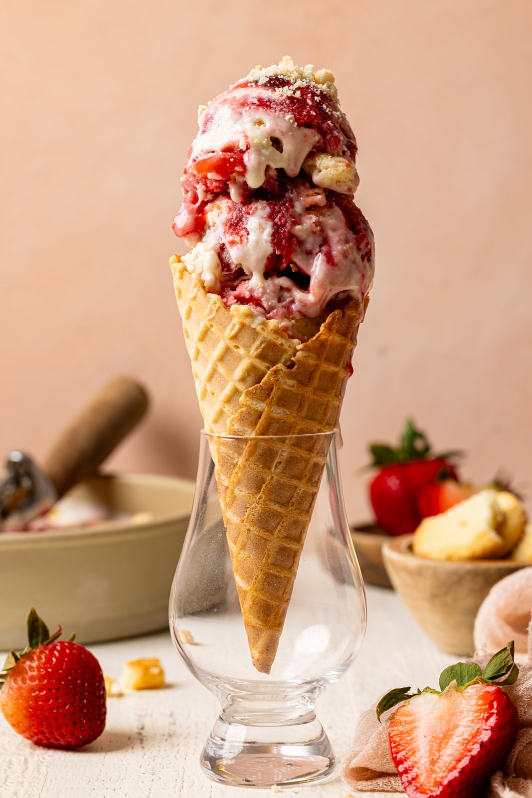 Ice cream cone in a glass with strawberries and cookies and a peach background.