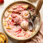 Ice cream in a container with scoops on a white wood table with strawberries and cookies.