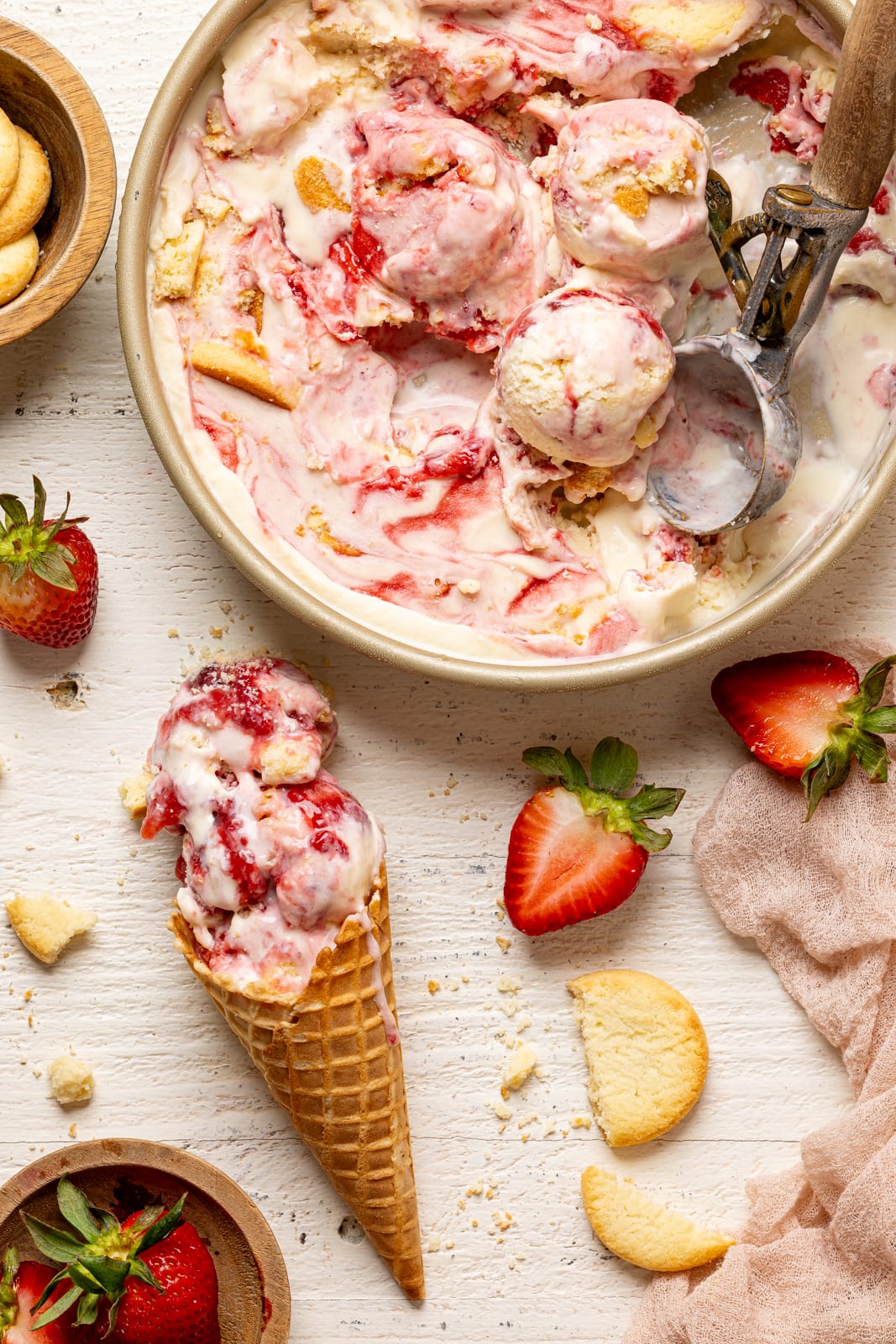 Ice cream cone with ice cream in a container with strawberries and cookies.