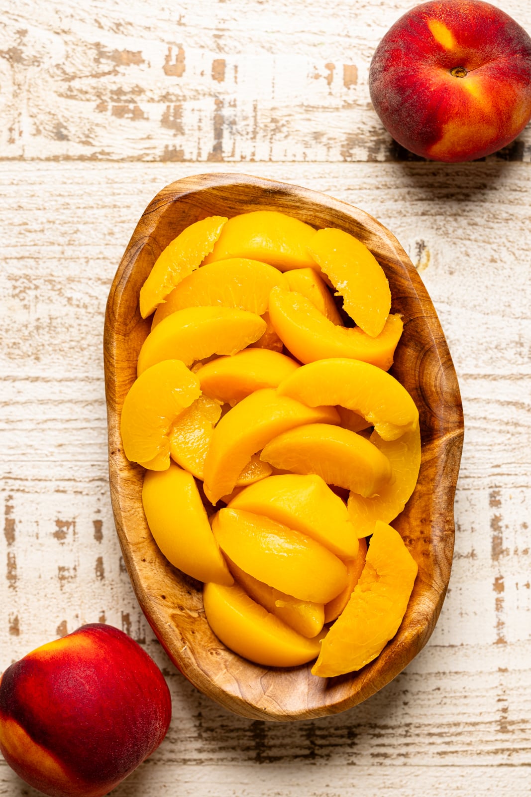 Bowl of sliced peaches on a white wood table. 