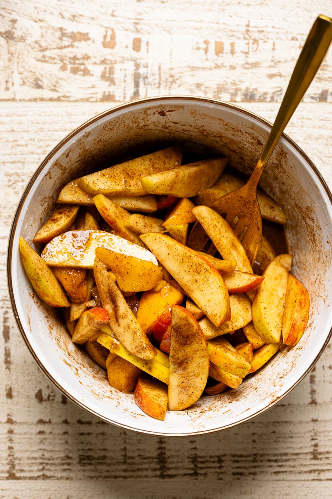 Bowl with apples and peaches and spices mixed together with a spoon.