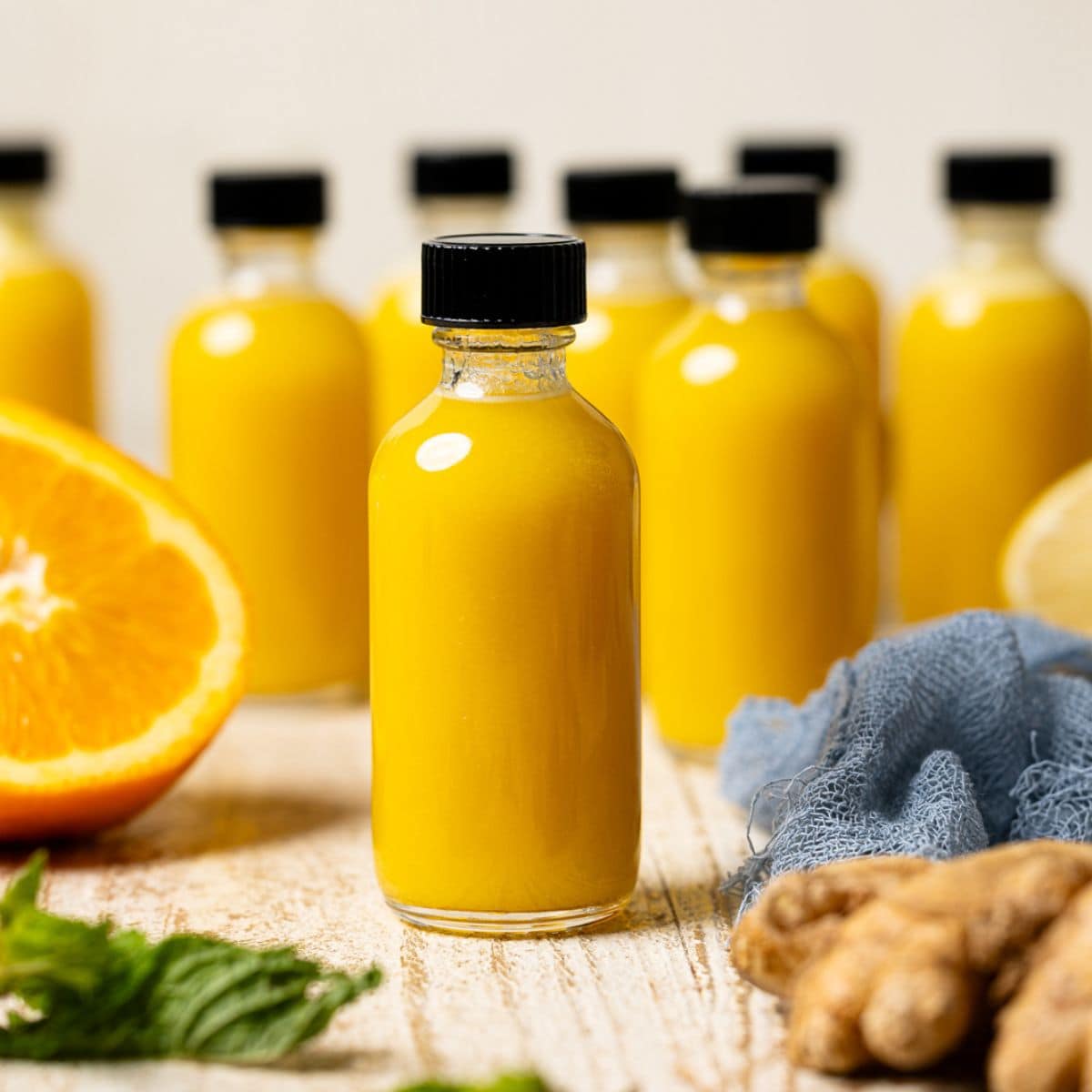 Juice in mini bottles on a white wood table with orange and ginger.