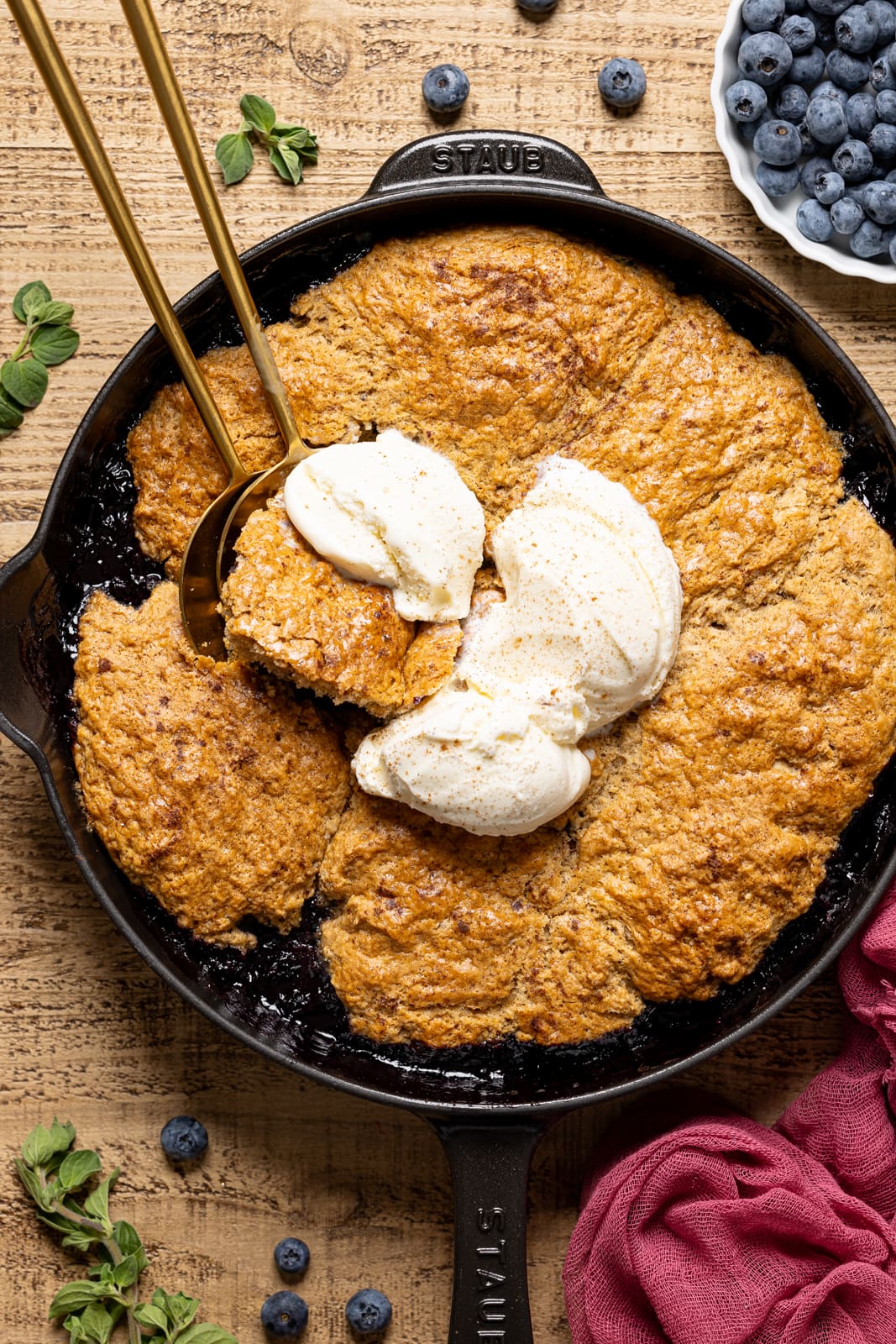 Baked cobbler in a skillet with scoops of ice cream and two spoons.