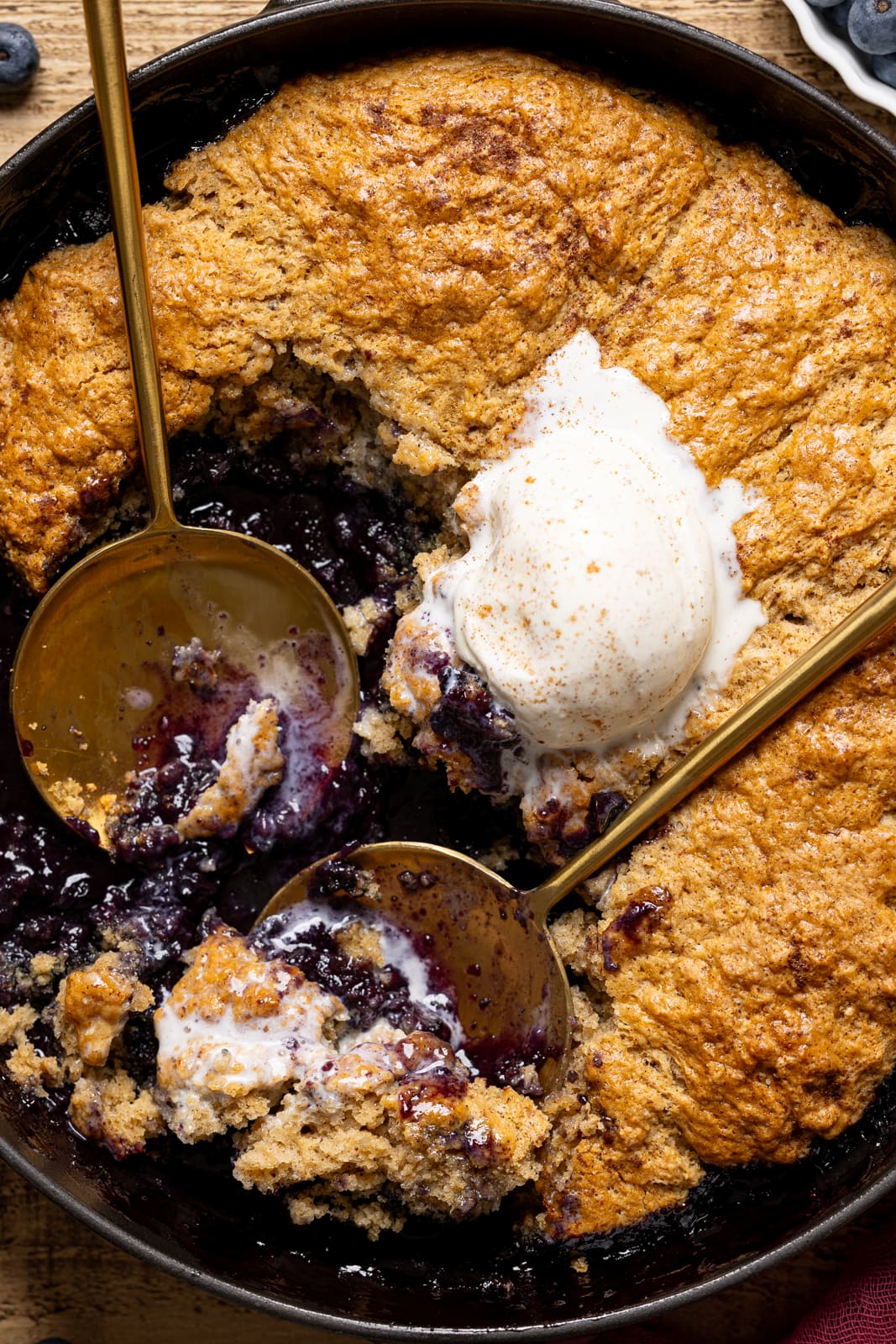 Cobbler in a black skillet with scoops of ice cream and two serving spoons.
